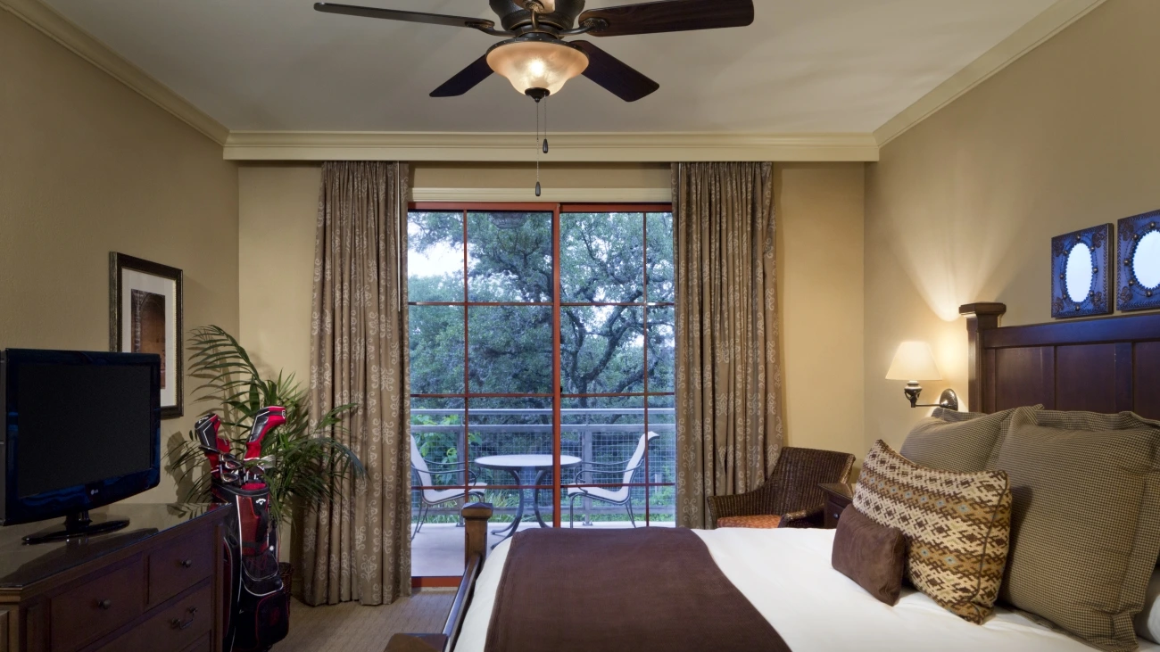 A bedroom with a bed, golf clubs, balcony, table, and chairs